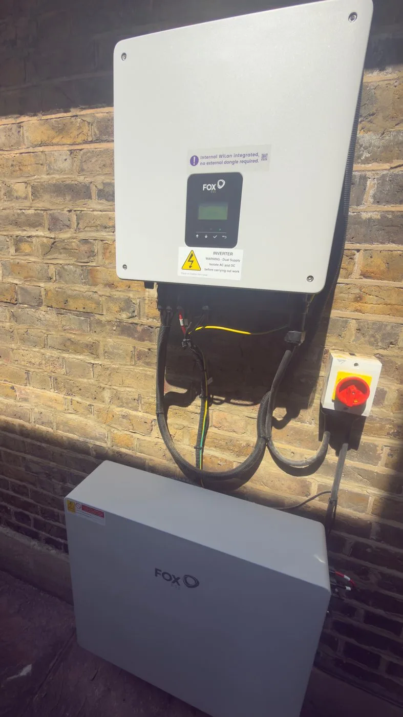 A Fox ESS inverter and battery installed on a brick wall in a British home, with the DC isolator, conduit and cabling as fitted