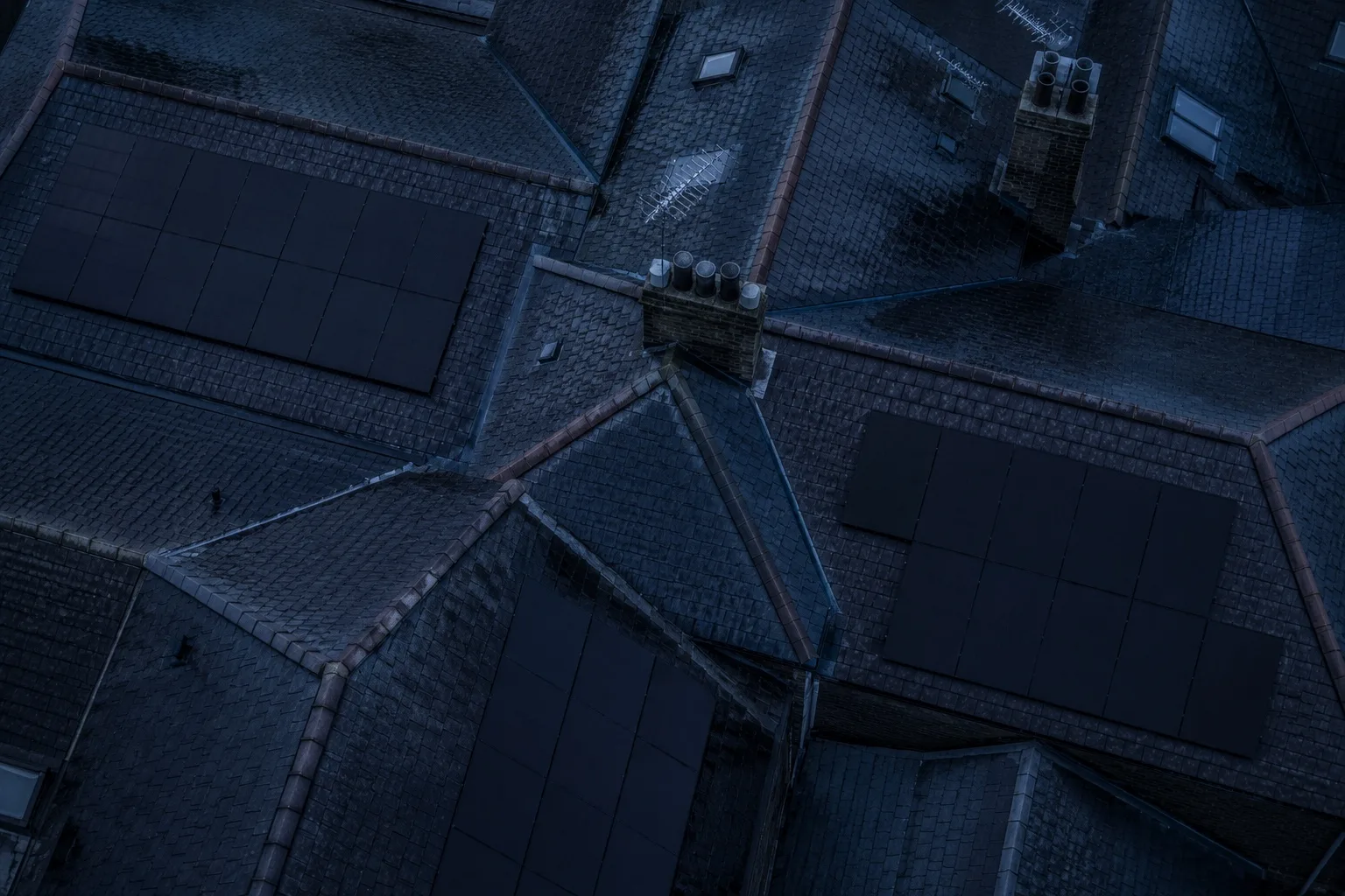 A full AIKO array on a modest British roof Aerial view at dusk over British terraced roofs, two of them carrying black solar arrays