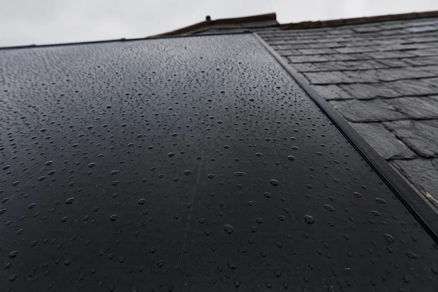 AIKO panels in real British weather and shade Matte black solar panels on a roof in heavy British rain, water running off the module edges