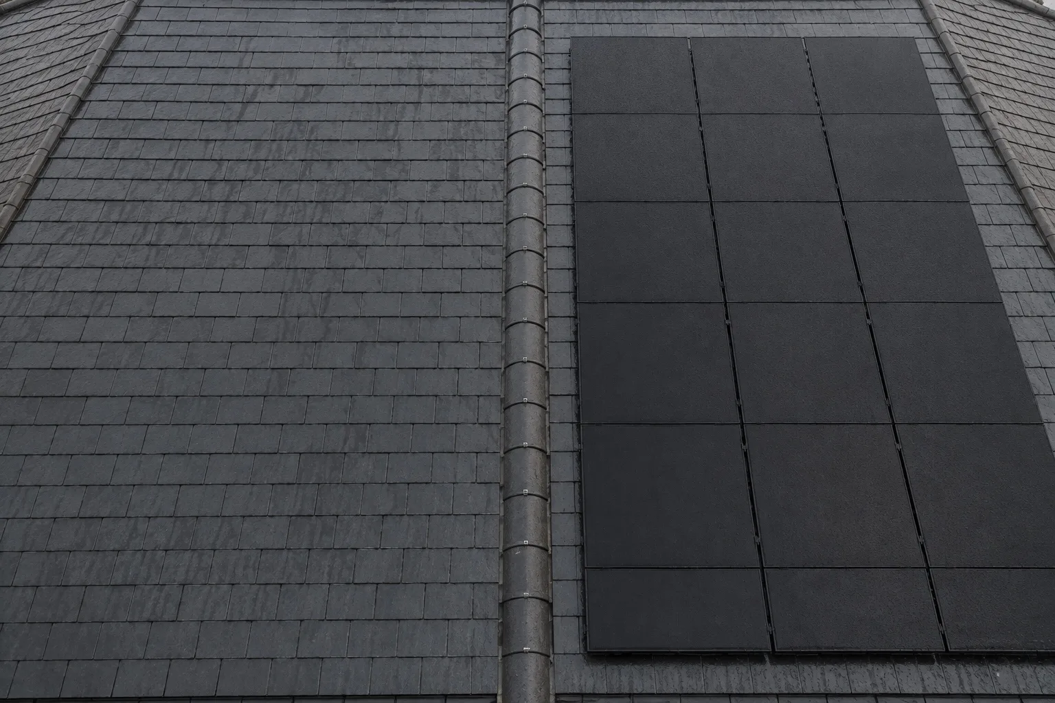 How AIKO solar panels power your home A British slate roof with matte black solar panels, seen from scaffold height, the cable conduit running to the eaves
