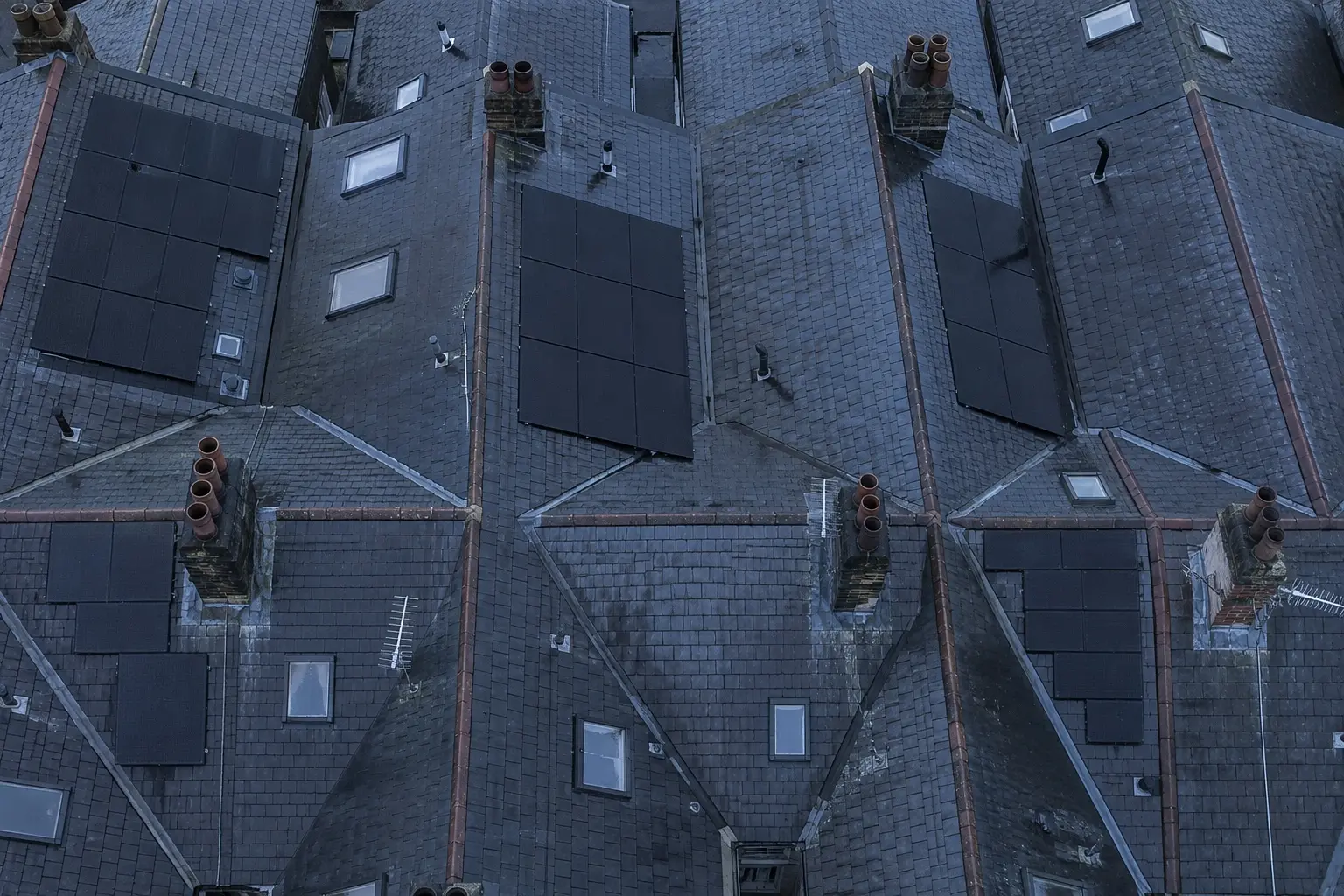 AIKO installs on real UK roofs A row of British terraced roofs seen from above, two carrying black solar arrays among bare slate