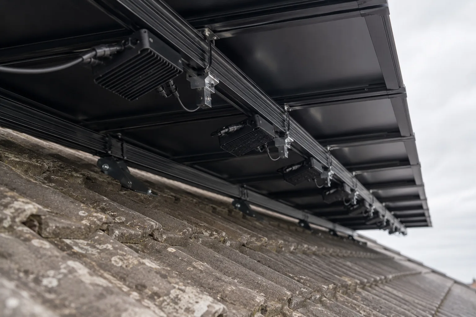 How Enphase microinverters power your home The underside of a roof solar array showing the mounting rail and a small plain microinverter beneath a module