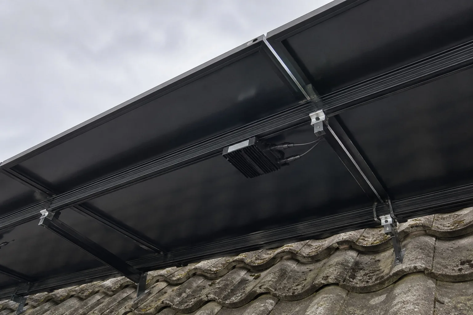 Enphase IQ8 microinverter close-up Looking along the underside of a part-installed solar array from the eaves, small units repeating beneath the modules
