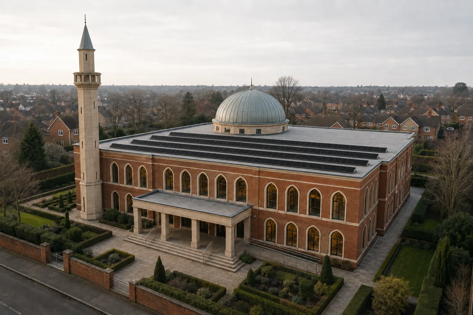 A British mosque seen from above in low winter light, tilted rows of black solar panels on its flat roof beneath a lead dome and a tall minaret