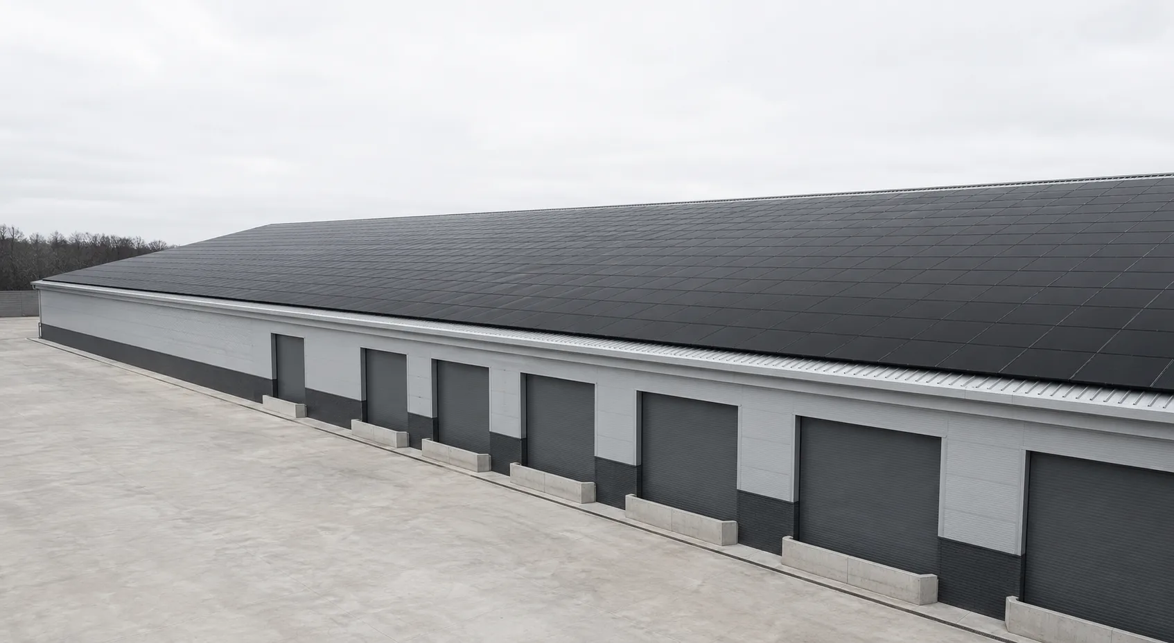 A British distribution warehouse on an overcast afternoon, its full roof covered edge to edge with black solar panels above closed roller shutter doors